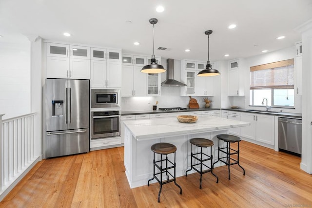 kitchen with wall chimney range hood, a center island, pendant lighting, stainless steel appliances, and white cabinets