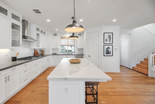 kitchen with pendant lighting, appliances with stainless steel finishes, a kitchen island, white cabinetry, and wall chimney range hood