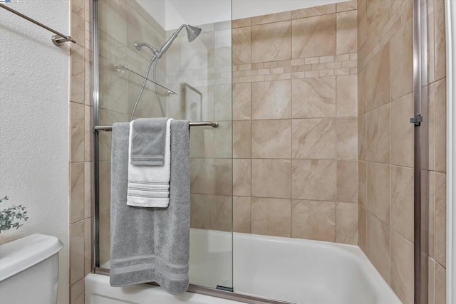 bathroom featuring toilet and shower / bath combination with glass door