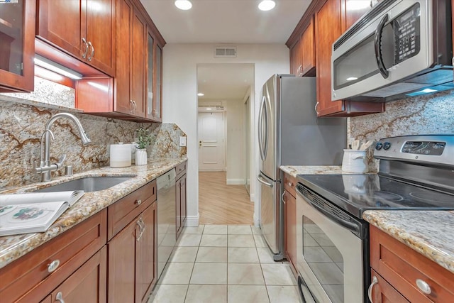 kitchen with light tile patterned flooring, sink, light stone counters, stainless steel appliances, and backsplash