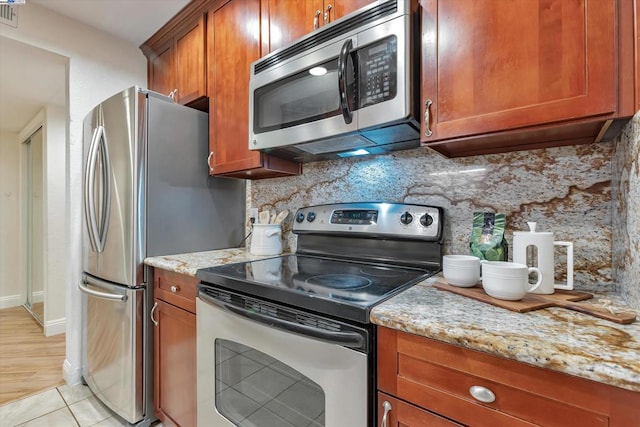 kitchen with light stone countertops, appliances with stainless steel finishes, light tile patterned flooring, and decorative backsplash