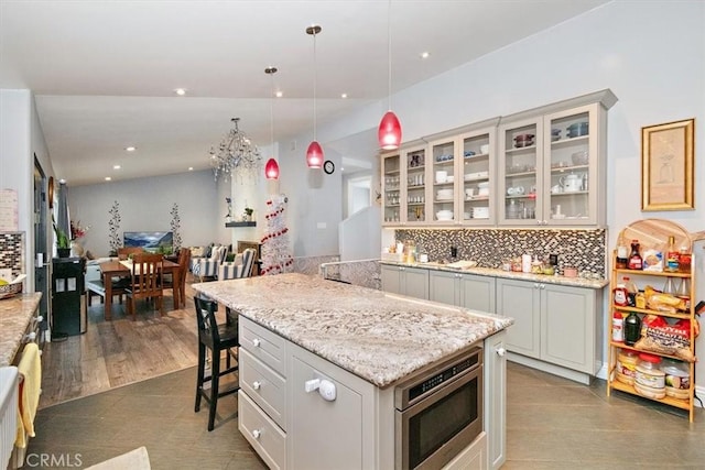 kitchen with stainless steel microwave, dark tile patterned flooring, pendant lighting, decorative backsplash, and a kitchen breakfast bar