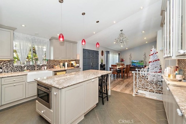 kitchen with stainless steel microwave, decorative light fixtures, lofted ceiling, light stone countertops, and a center island