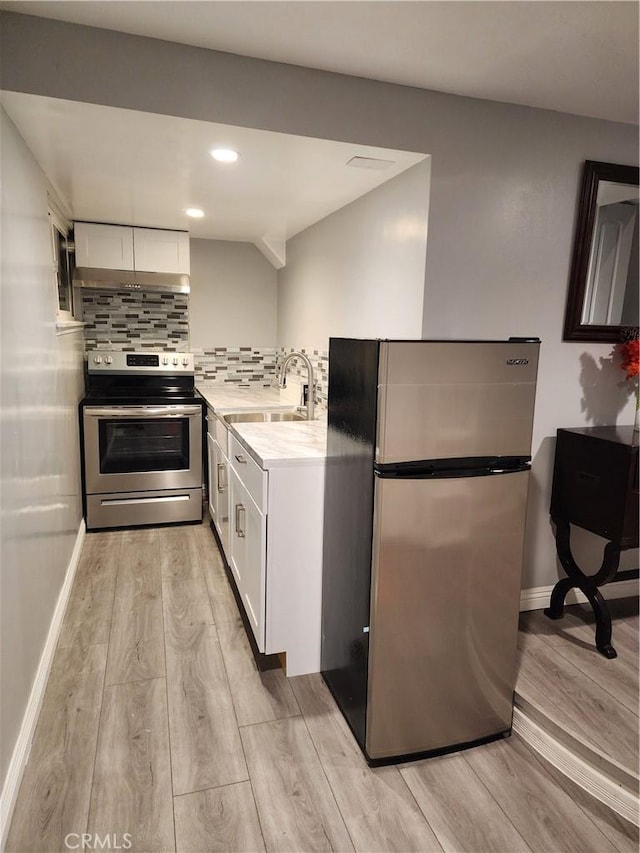 kitchen featuring white cabinets, stainless steel appliances, light hardwood / wood-style floors, sink, and backsplash