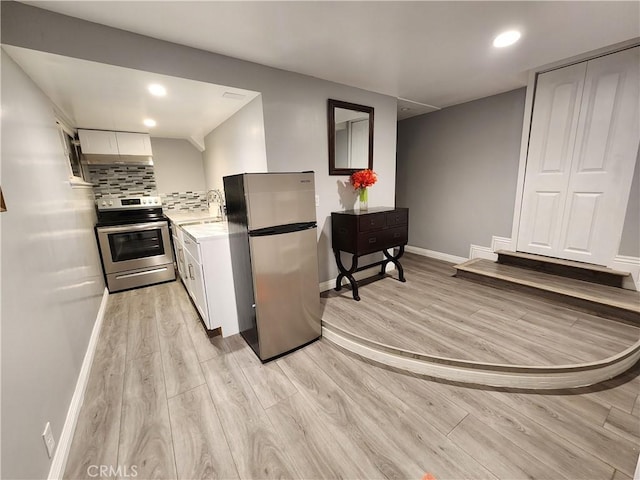 kitchen with decorative backsplash, appliances with stainless steel finishes, white cabinetry, and light hardwood / wood-style floors