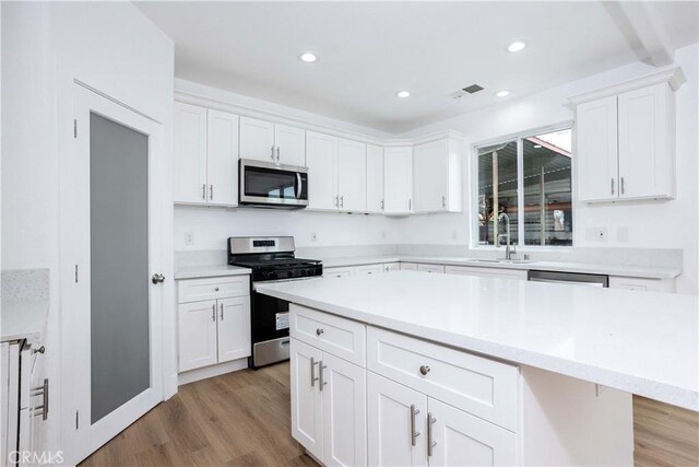 kitchen featuring a kitchen island, sink, white cabinetry, light hardwood / wood-style flooring, and appliances with stainless steel finishes