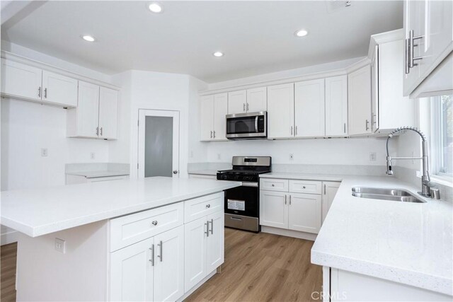 kitchen with appliances with stainless steel finishes, white cabinets, a kitchen island, light hardwood / wood-style flooring, and sink