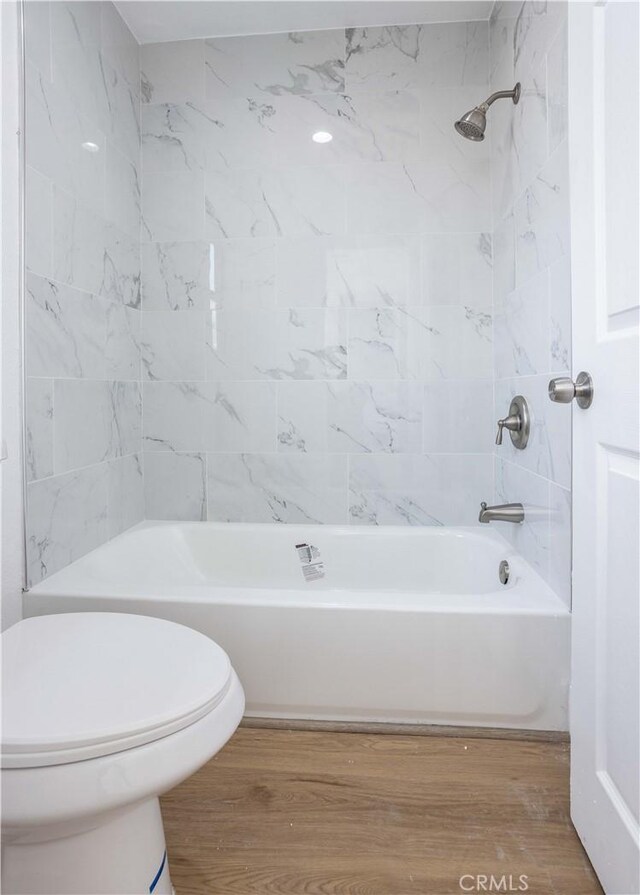 bathroom featuring hardwood / wood-style flooring, toilet, and tiled shower / bath