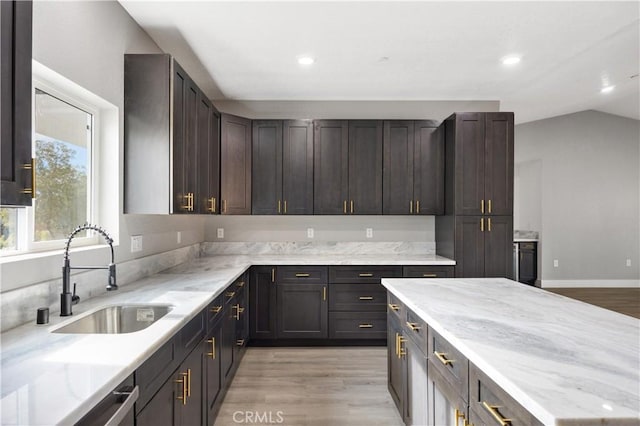 kitchen featuring dark brown cabinetry, sink, vaulted ceiling, and light stone countertops