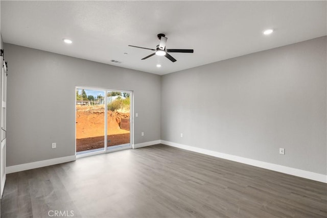 unfurnished room with ceiling fan, wood-type flooring, and a barn door