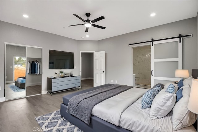 bedroom featuring hardwood / wood-style floors, ceiling fan, a barn door, ensuite bath, and a closet