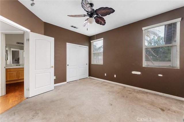 unfurnished bedroom featuring ceiling fan, multiple windows, light carpet, and connected bathroom