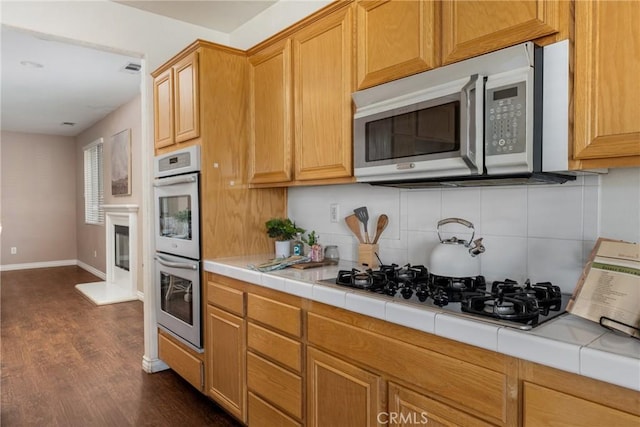 kitchen featuring stainless steel appliances, tile countertops, decorative backsplash, and dark hardwood / wood-style floors