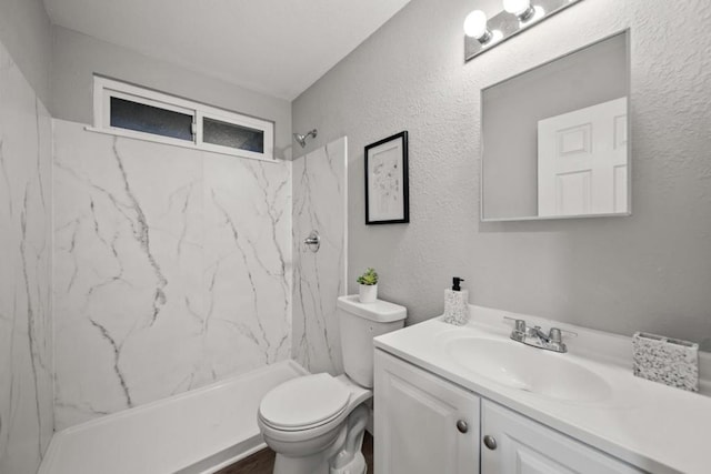 bathroom featuring a tile shower, vanity, and toilet