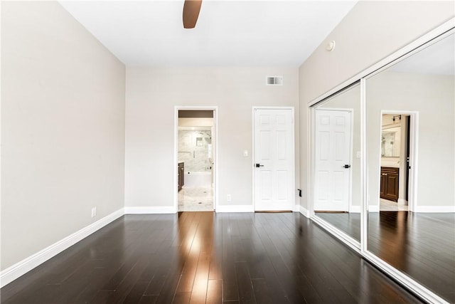 unfurnished bedroom with ceiling fan, dark wood-type flooring, ensuite bathroom, and a closet