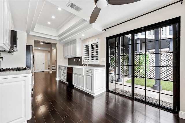 kitchen featuring crown molding, a tray ceiling, black dishwasher, dark wood-type flooring, and white cabinets