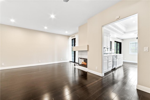 unfurnished living room with a multi sided fireplace, sink, a tray ceiling, and dark hardwood / wood-style flooring