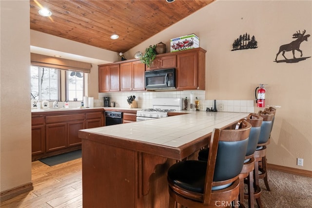 kitchen with white range with gas stovetop, kitchen peninsula, tile counters, backsplash, and light hardwood / wood-style flooring