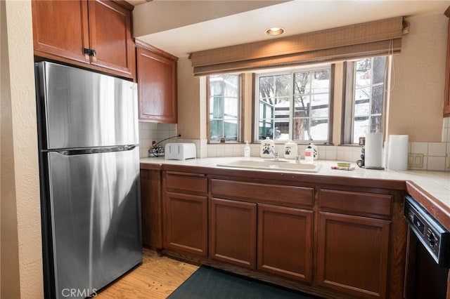 kitchen featuring tile countertops, stainless steel fridge, dishwasher, light hardwood / wood-style flooring, and sink