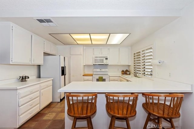 kitchen featuring kitchen peninsula, sink, white appliances, a breakfast bar area, and white cabinets