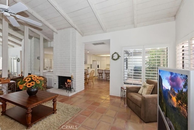 living room with beamed ceiling, ceiling fan, a brick fireplace, wooden ceiling, and light tile patterned floors