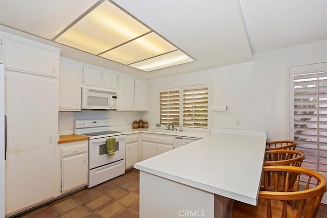 kitchen with sink, white cabinets, kitchen peninsula, and white appliances