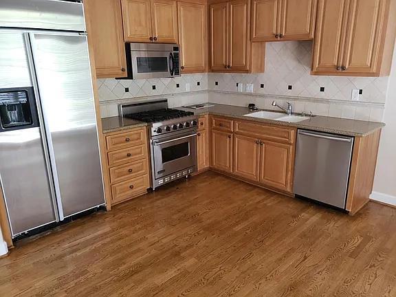 kitchen featuring high end appliances, sink, decorative backsplash, and dark wood-type flooring