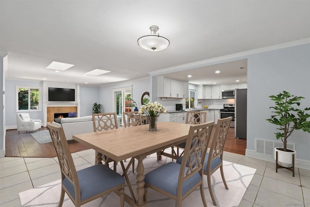 dining space featuring plenty of natural light, a skylight, light tile patterned floors, and crown molding