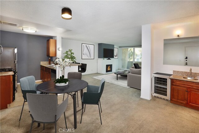 carpeted dining room featuring sink, a textured ceiling, beverage cooler, and a fireplace