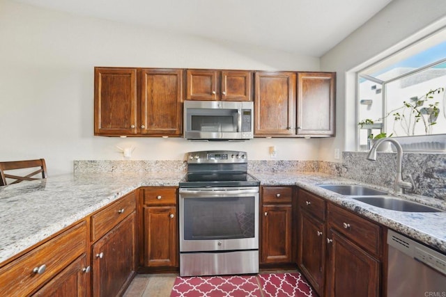 kitchen featuring vaulted ceiling, appliances with stainless steel finishes, light stone counters, and sink