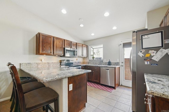 kitchen with appliances with stainless steel finishes, a kitchen bar, sink, kitchen peninsula, and light stone counters