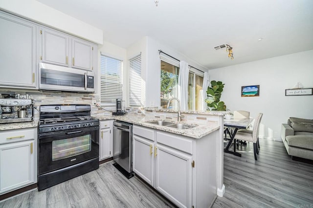 kitchen featuring appliances with stainless steel finishes, sink, backsplash, kitchen peninsula, and light wood-type flooring