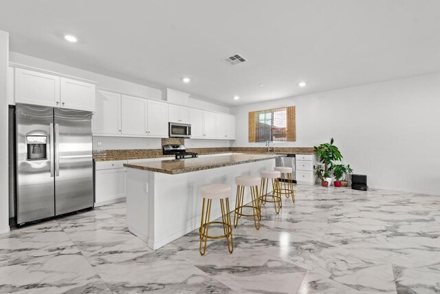 kitchen with a kitchen breakfast bar, stainless steel appliances, white cabinetry, and a center island