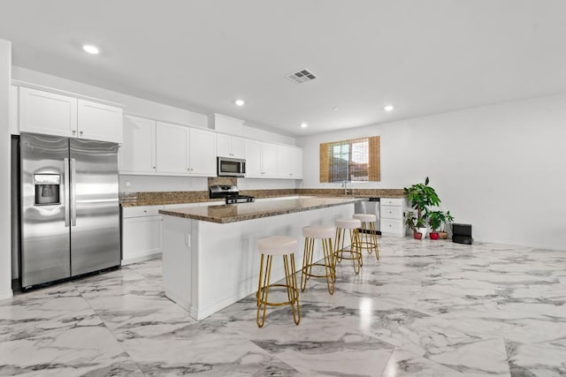 kitchen featuring a kitchen breakfast bar, appliances with stainless steel finishes, white cabinetry, and a kitchen island