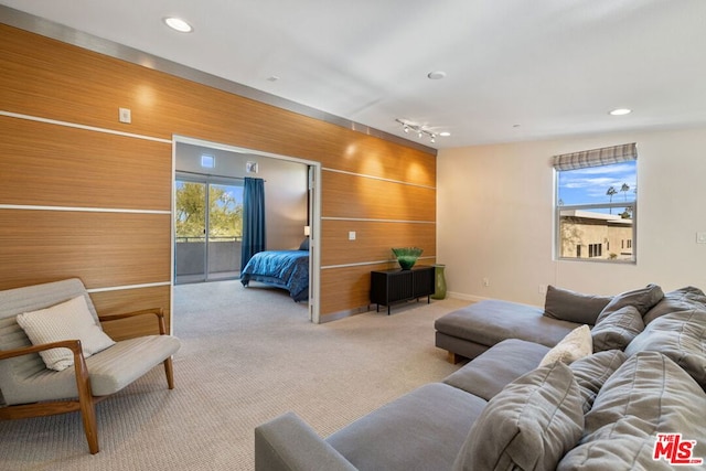 living room featuring light carpet, track lighting, and wooden walls