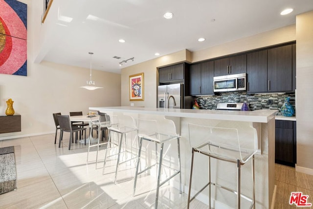 kitchen with a kitchen bar, tasteful backsplash, a center island with sink, appliances with stainless steel finishes, and pendant lighting