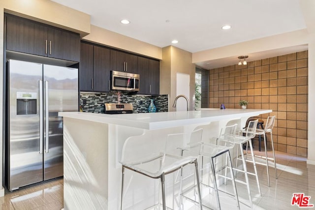 kitchen with light tile patterned floors, backsplash, a breakfast bar area, and appliances with stainless steel finishes