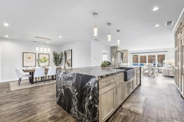 kitchen with decorative light fixtures, dark stone countertops, sink, dark hardwood / wood-style floors, and a center island with sink