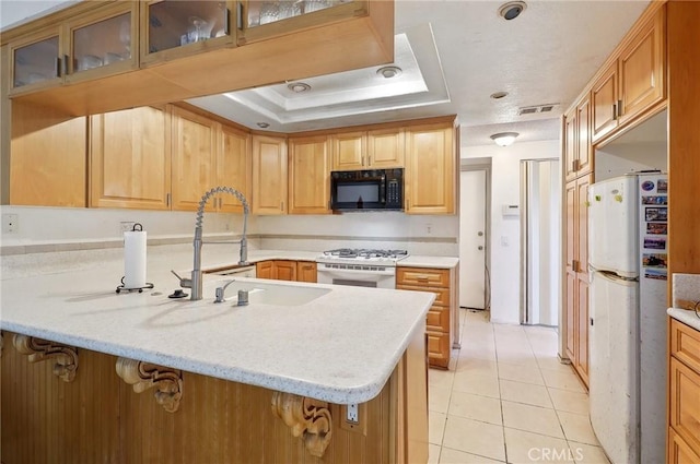 kitchen with a tray ceiling, light tile patterned floors, white appliances, and kitchen peninsula