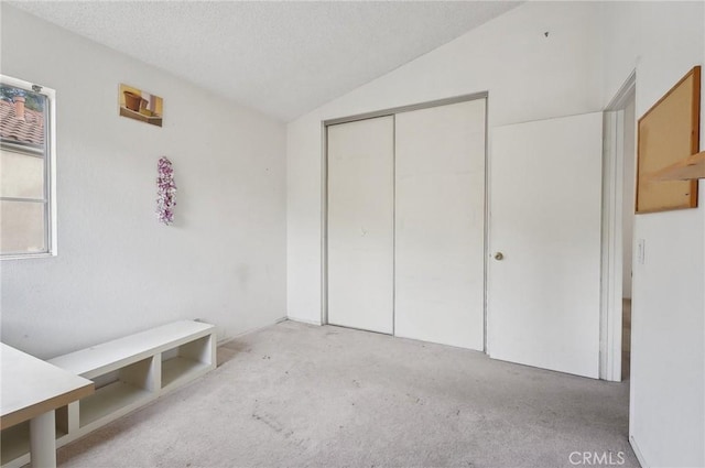 unfurnished bedroom with light colored carpet, lofted ceiling, a closet, and a textured ceiling