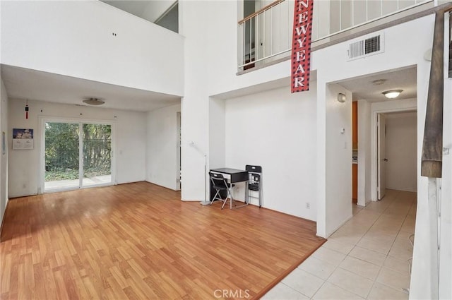 unfurnished living room featuring light wood-type flooring, visible vents, and a towering ceiling
