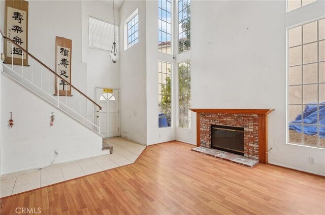 foyer entrance with a brick fireplace, a towering ceiling, and light hardwood / wood-style floors