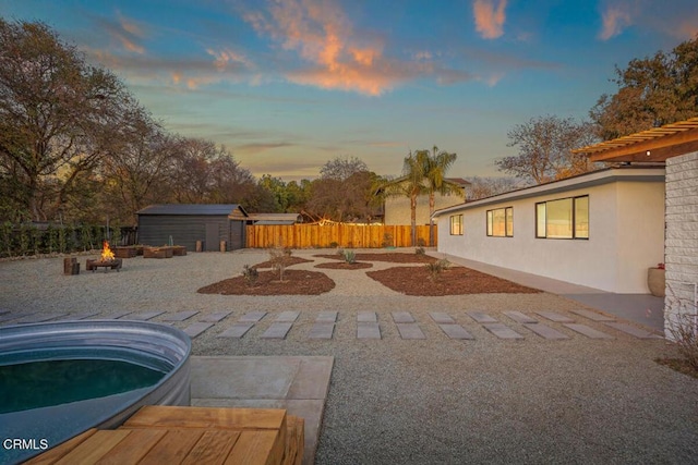 pool at dusk featuring an outdoor fire pit, a storage shed, and a patio