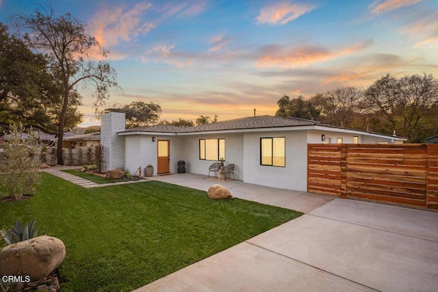 back house at dusk featuring a yard and a patio