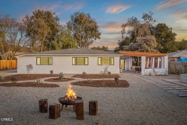 back of house at dusk featuring an outdoor fire pit, a patio, fence, a pergola, and stucco siding