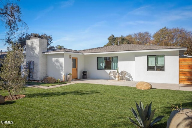 rear view of property with fence, a yard, stucco siding, a chimney, and a patio area