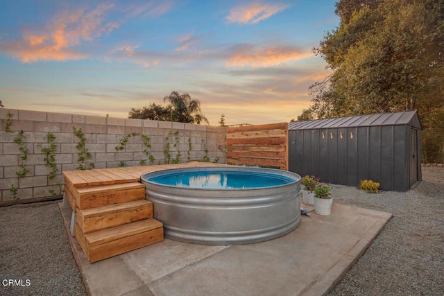 pool at dusk featuring a fenced backyard, an outdoor structure, a jacuzzi, and a shed