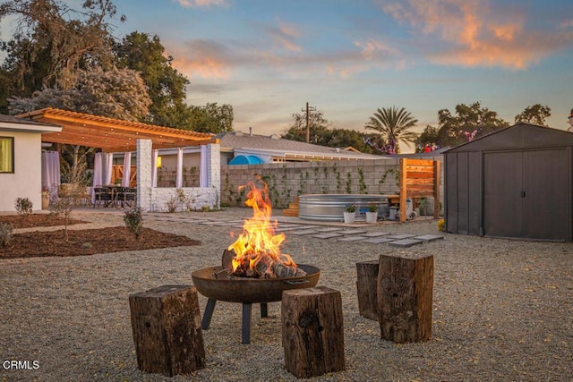 patio terrace at dusk with a fire pit, an outbuilding, a storage unit, fence, and a pergola