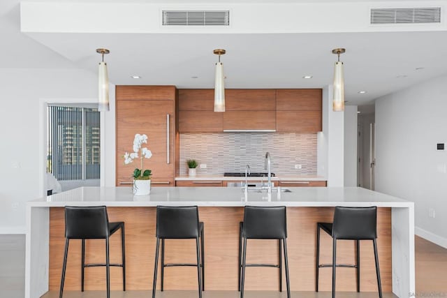 kitchen with pendant lighting, tasteful backsplash, a kitchen breakfast bar, and an island with sink