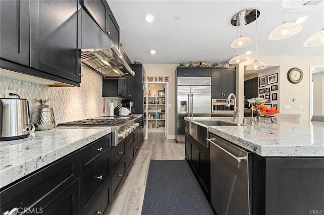 kitchen featuring stainless steel appliances, tasteful backsplash, decorative light fixtures, light stone countertops, and light hardwood / wood-style flooring